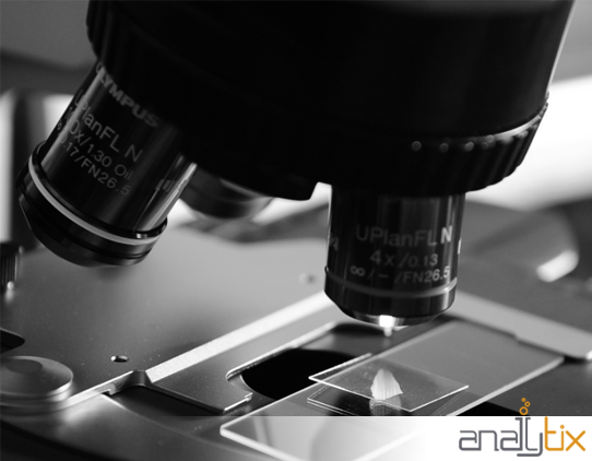 A black and white, close up photograph of the lens of a microscope. At the bottom of the photograph is the Analytix logo over a white band.