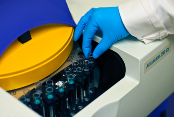 Close up image of vials being placed into an instrument by a gloved hand.