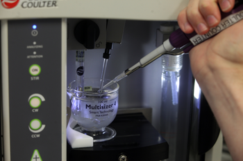 Close up image of a hand pipetting clear, colourless liquid into or out of a vessel within an instrument.