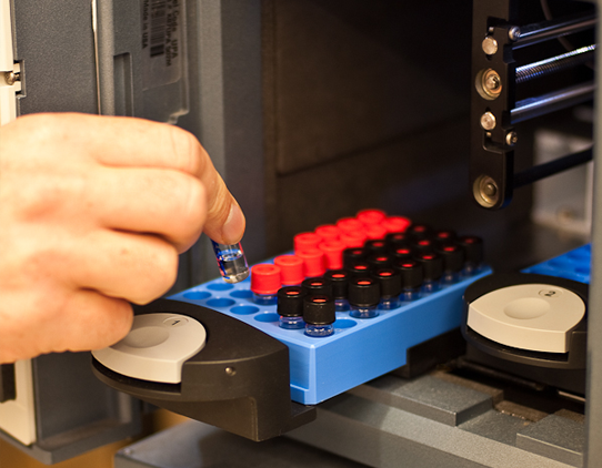 A close up image of a hand placing a vial into an instrument.