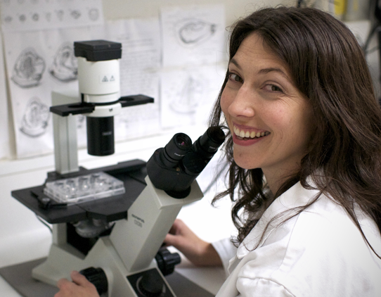 A scientist wearing a white labcoat is working at a microscope.