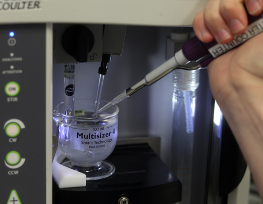 Close up image of a hand pipetting clear, colourless liquid into or out of a vessel within an instrument.