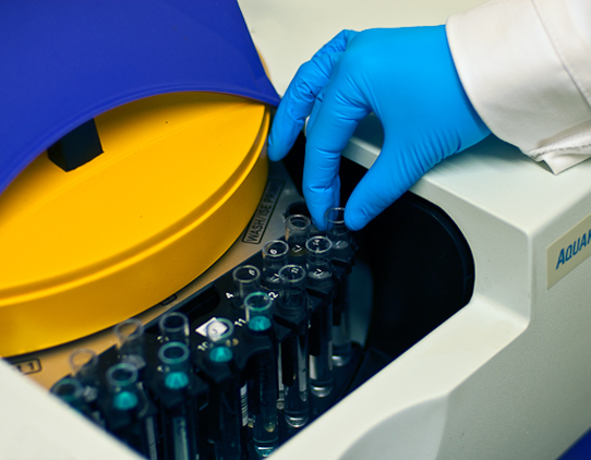 Close up image of vials being placed into an instrument by a gloved hand.