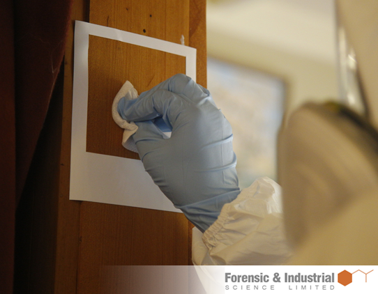A close up photograph of a technician taking a swab sample of an area of timber. The technician is wearing full protective gear.