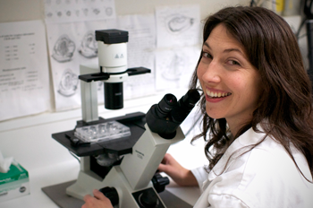 A scientist wearing a white labcoat is working at a microscope.